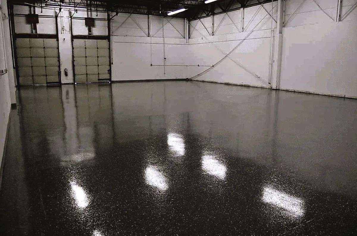 A warehouse bay with a gray speckled epoxy floor reflecting the overhead strip lights and the loading doors
