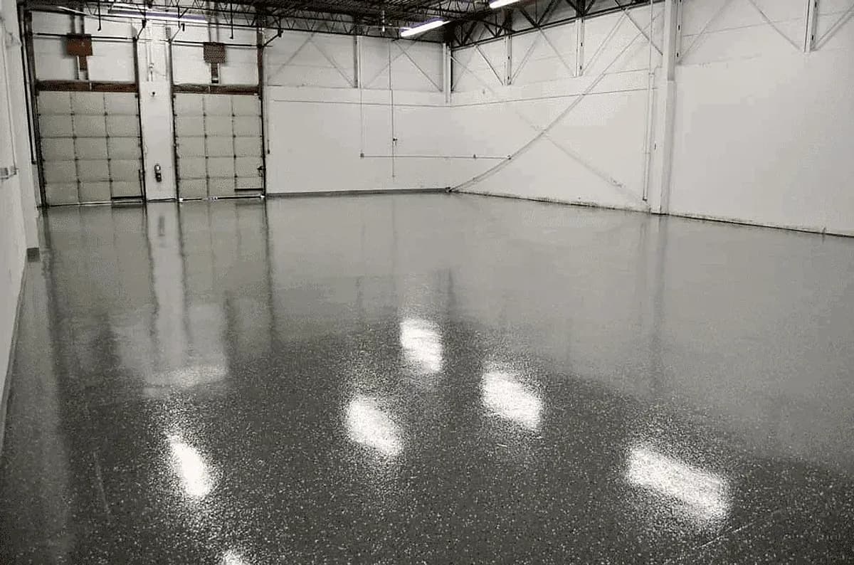A warehouse bay with a gray speckled epoxy floor reflecting the overhead strip lights and the loading doors