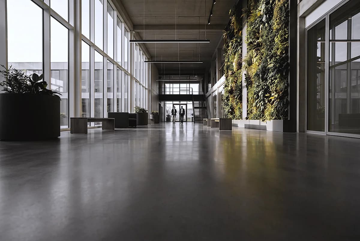 A daylight-filled office atrium with large planters and a warm gray polished concrete floor