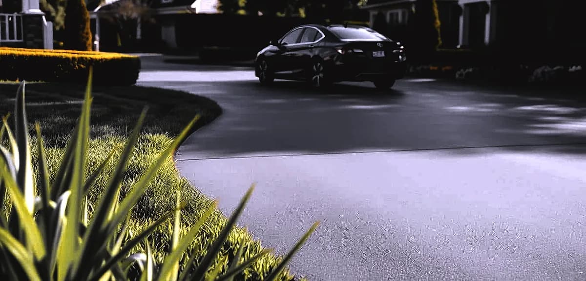 A freshly resurfaced concrete driveway, its smooth charcoal-gray surface gleaming in the warm afternoon sunlight.