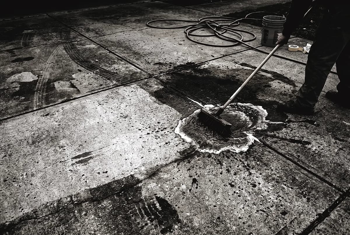 Scrubbing an oil stain out of concrete with a stiff brush