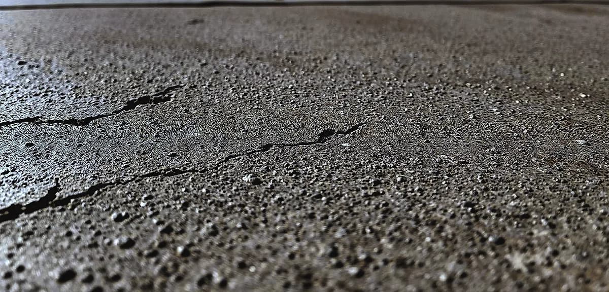 A close-up view of a concrete surface, textured and worn, with small cracks and discoloration.