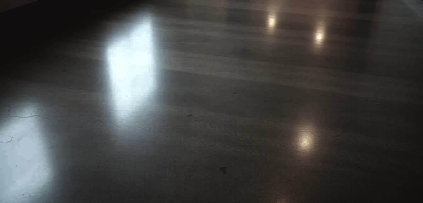 A polished concrete floor, gleaming with a lustrous sheen, illuminated by soft, diffused lighting that casts a warm, inviting ambiance.