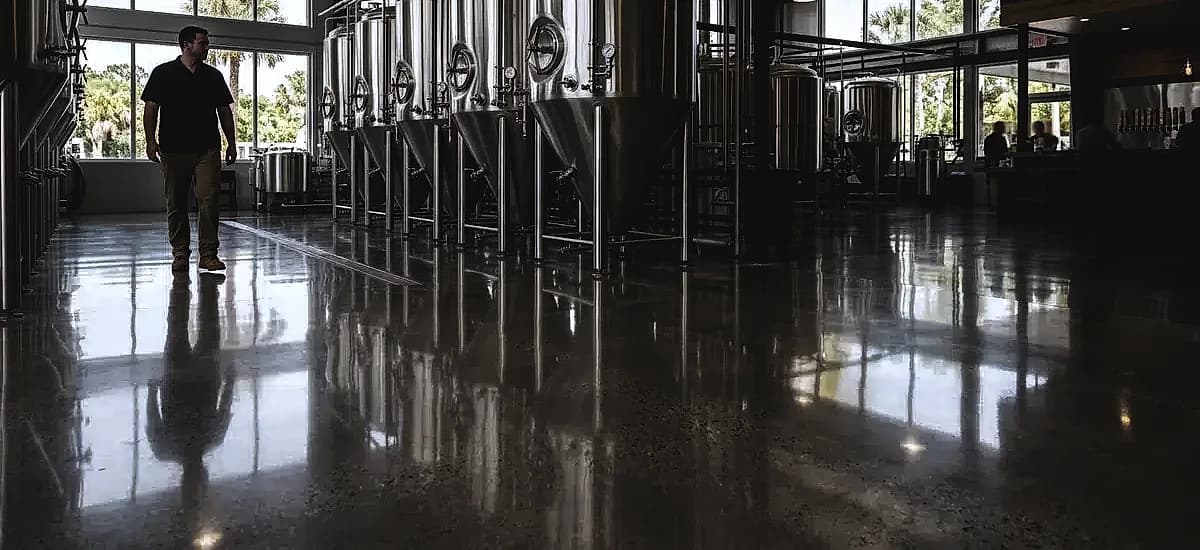 A pristine polished concrete floor in a South Florida craft brewery, showing stainless steel fermentation tanks reflecting on the smooth surface.
