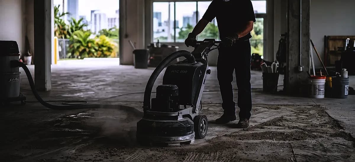 Technician using a walk-behind diamond grinder to prepare a concrete floor for epoxy repair in Miami