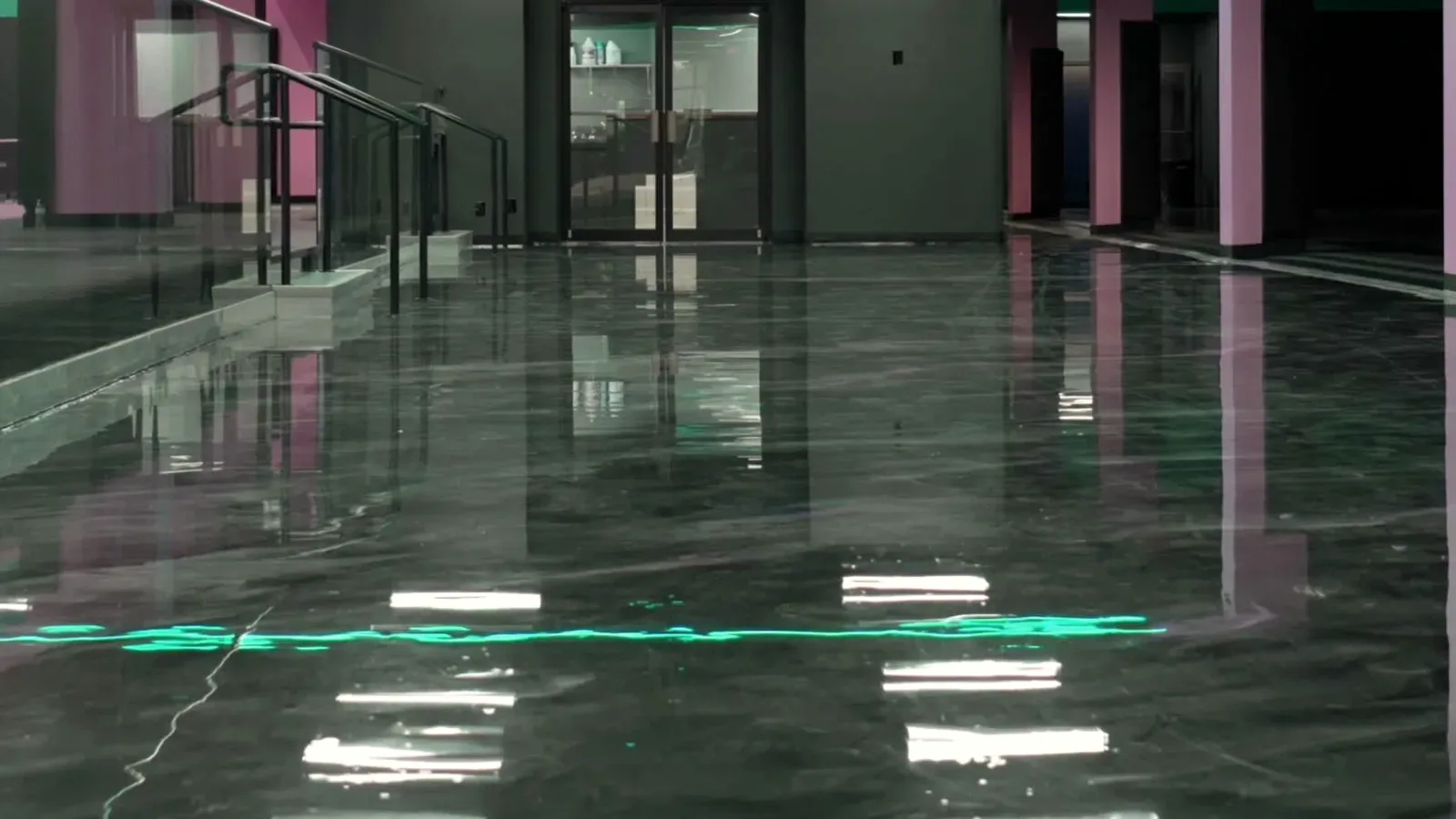 A finished dark metallic epoxy floor running the length of a commercial corridor, ceiling lights mirrored in it