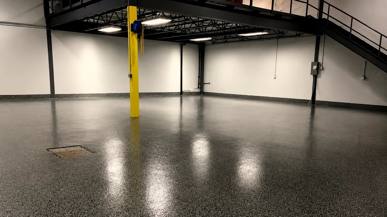 Flake epoxy floor under a steel mezzanine in a plant, reflecting the overhead lights