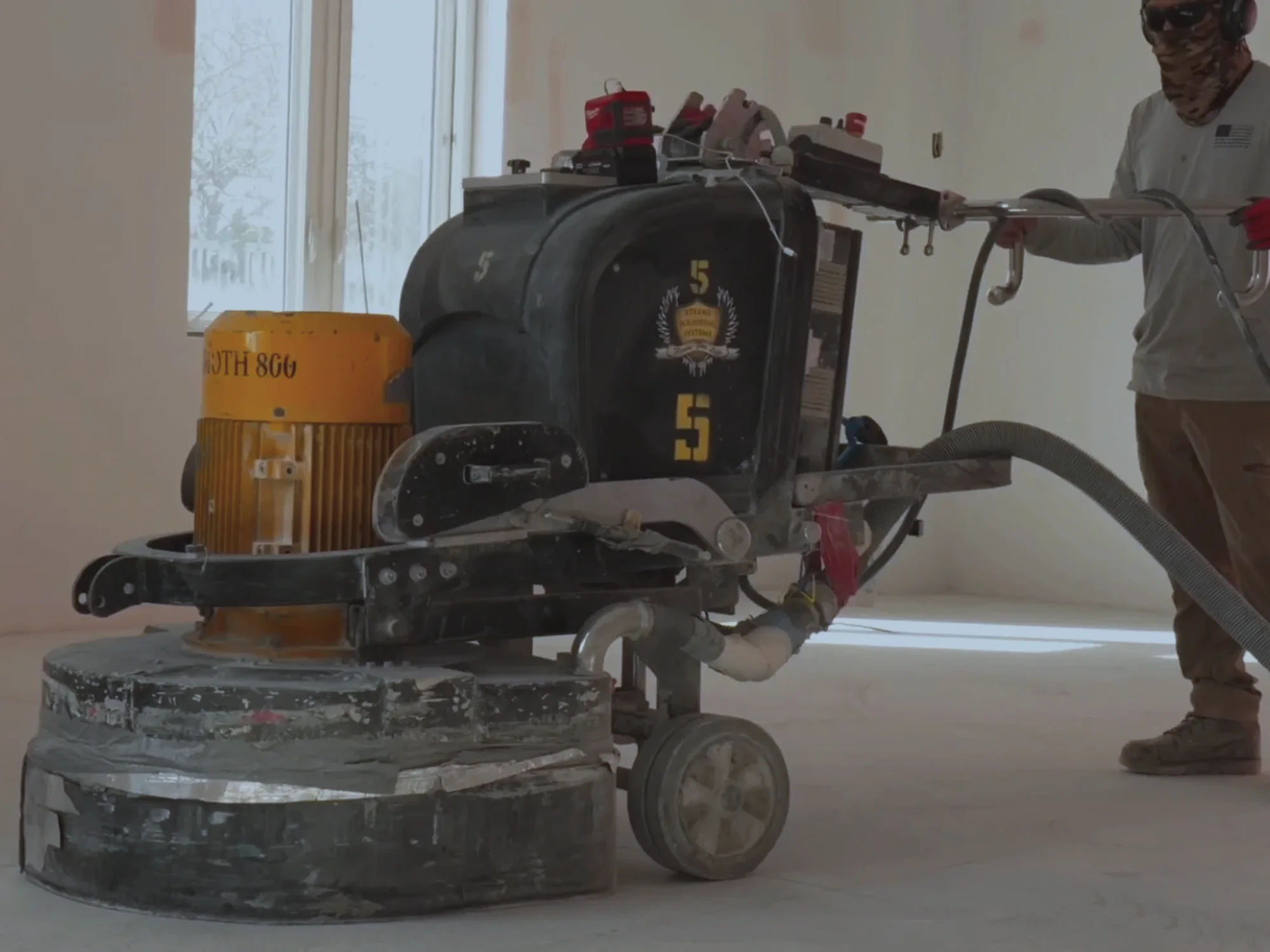 Crew member running a floor grinder with its dust extraction hose and vacuum attached