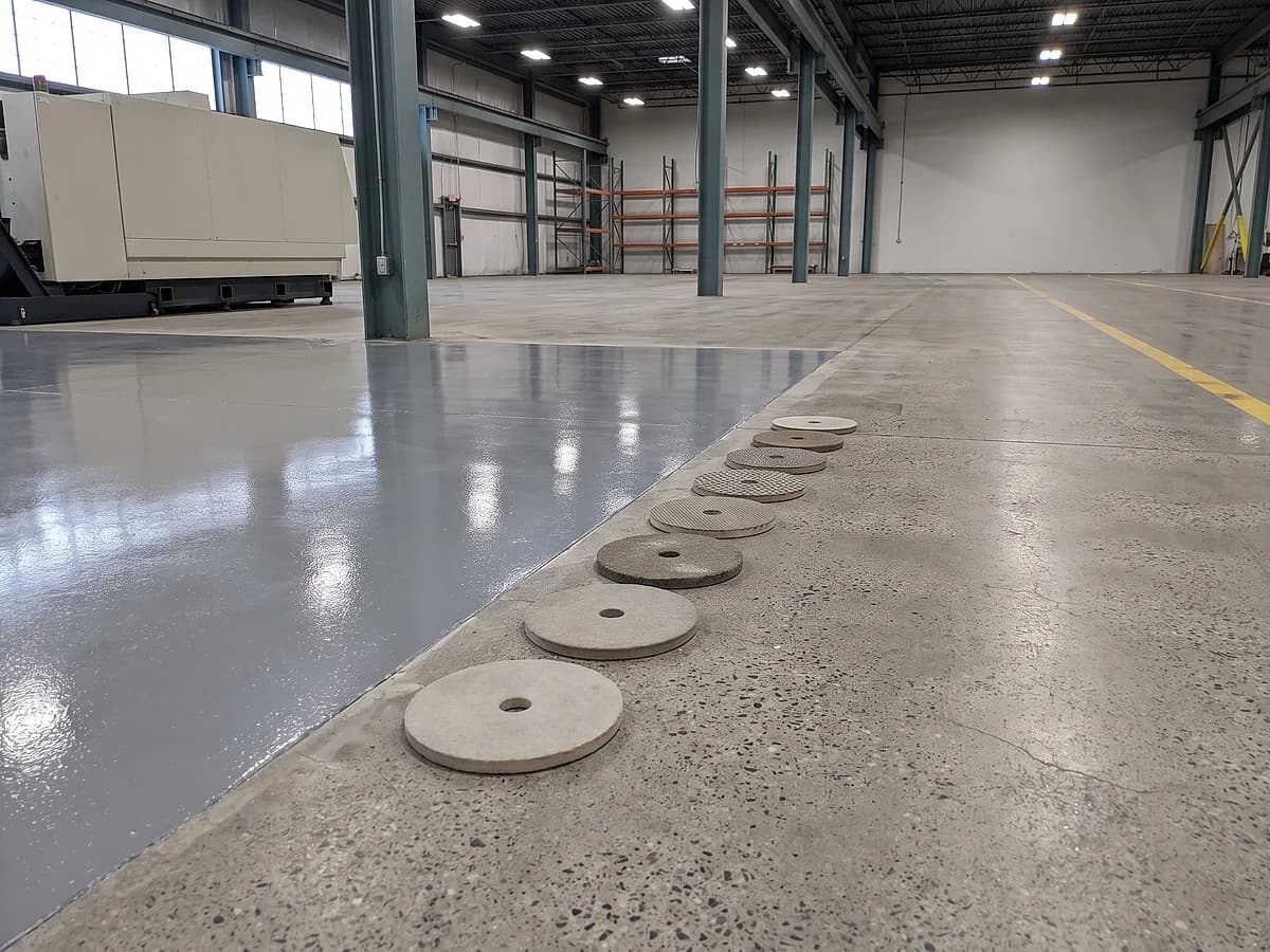 A working line across a factory floor with the near side taken several polishing passes further than the far side, a row of diamond pads laid out coarse to fine beside it