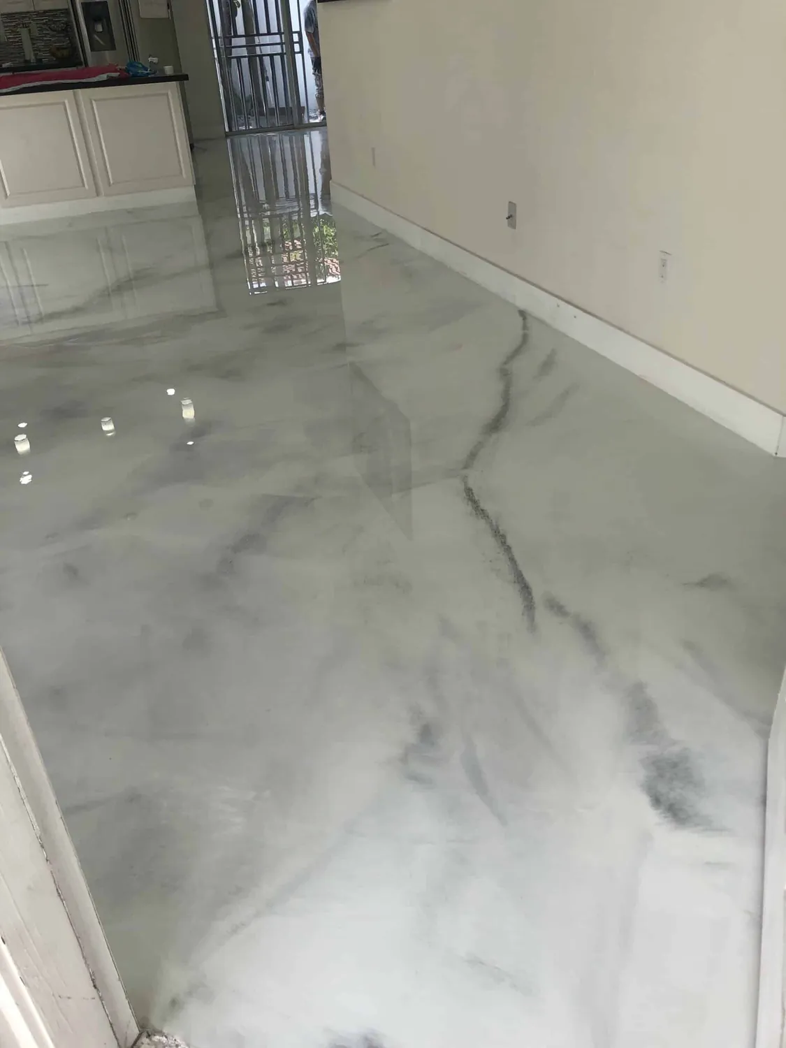 A white metallic floor running out of a kitchen into the next room, its grey veins reading like cut stone