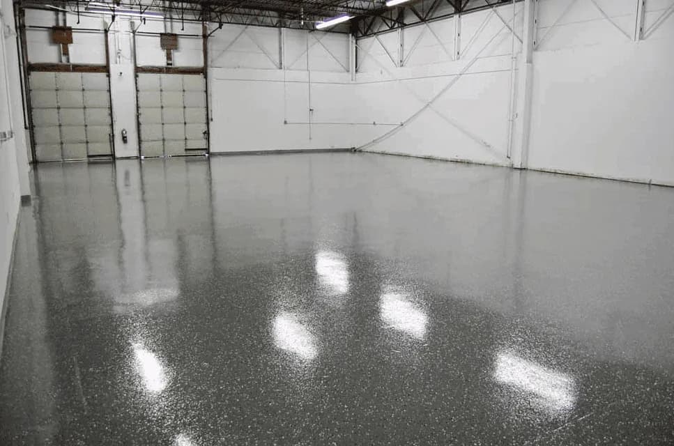 A pale grey flake floor in a unit with roller doors along one wall, holding the reflection of the ceiling lights