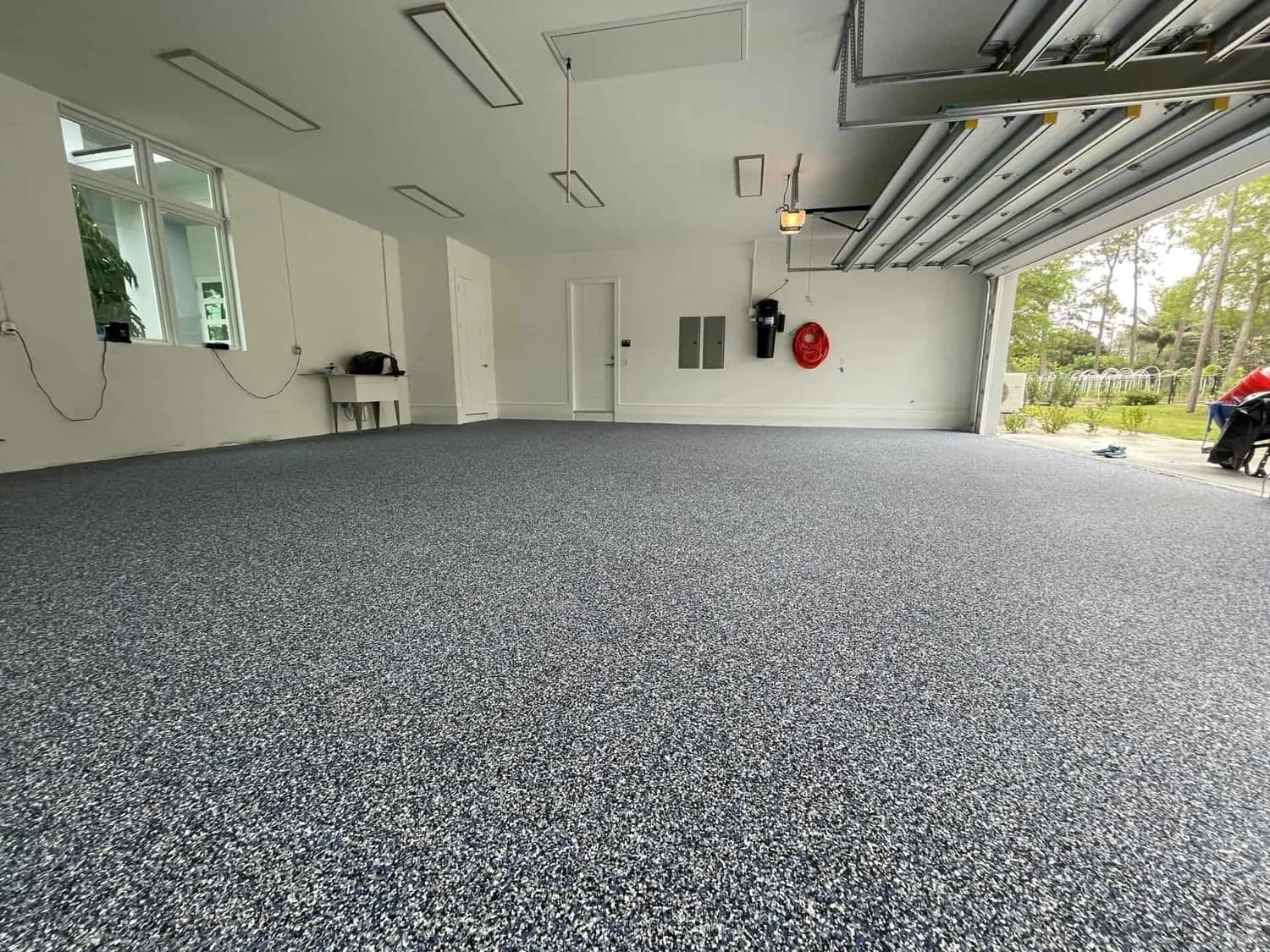 A blue-grey flake floor filling a garage bay with the door rolled up to the garden behind it
