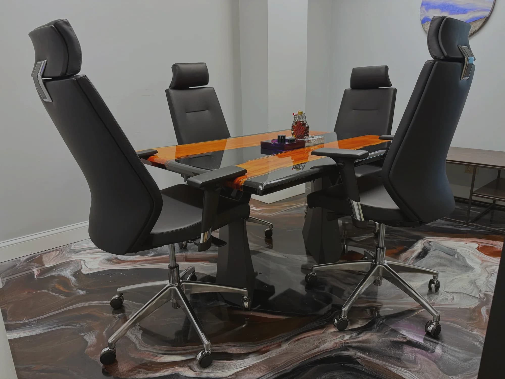 A conference room with black leather chairs around a resin-topped table on a gray-brown metallic floor