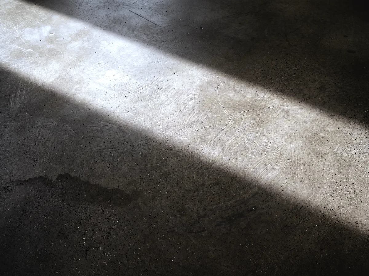 A burnished concrete floor: the slab left closed and unopened, buffed to a soft even lustre with wide overlapping pad arcs across it.