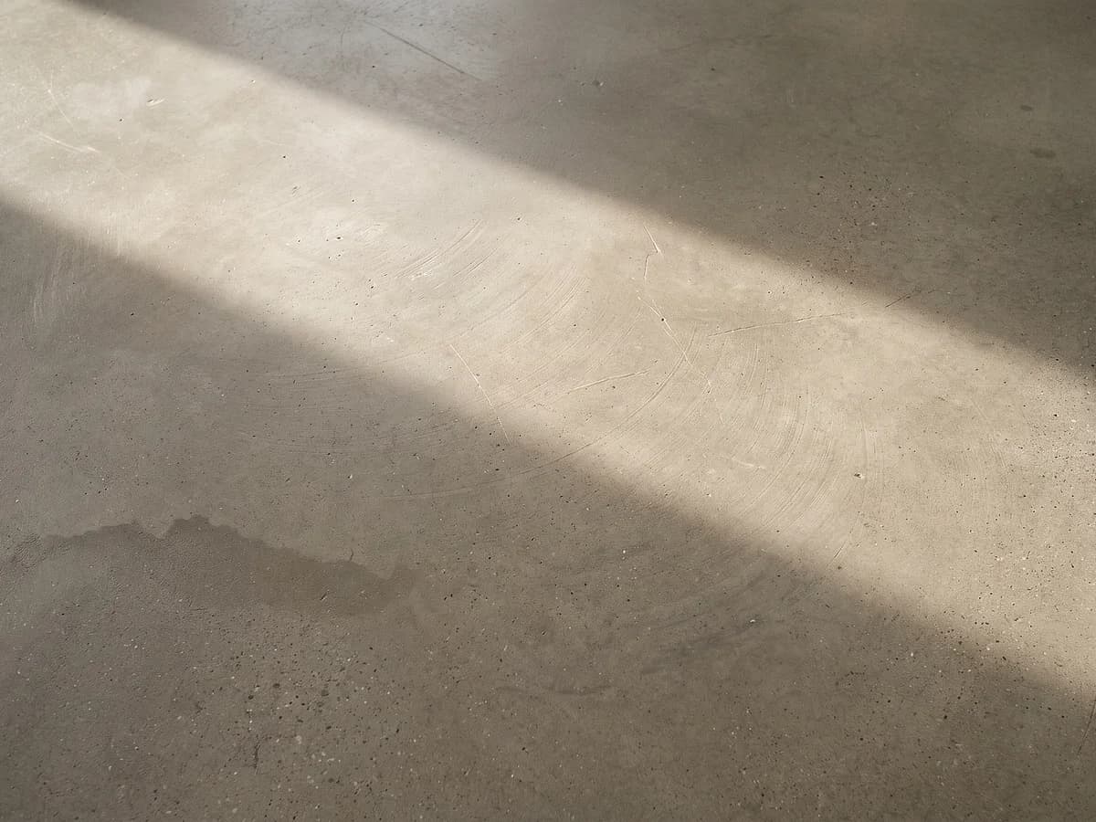 A burnished concrete floor: the slab left closed and unopened, buffed to a soft even lustre with wide overlapping pad arcs across it.