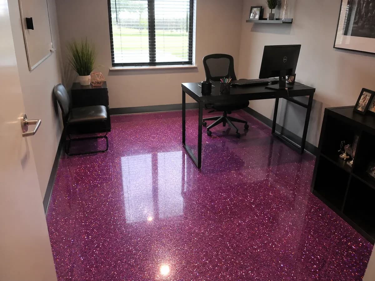 A glitter floor in a private office: fine metallic flake broadcast into a deep magenta resin under a full-gloss topcoat, running wall to wall past a desk and chair.