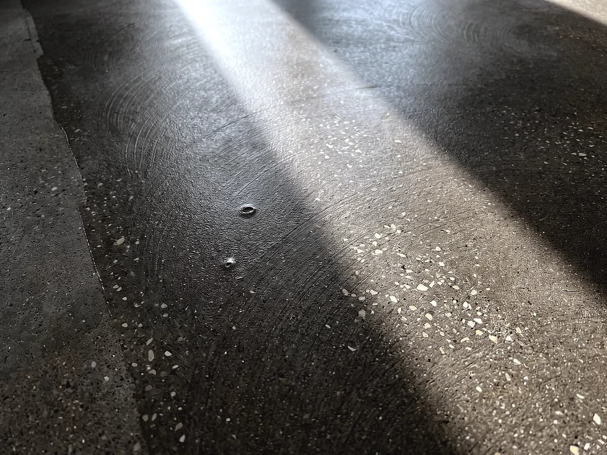 A lightly ground concrete floor under a topical sealer film, the grinder's overlapping arcs still faintly readable through the satin coat.