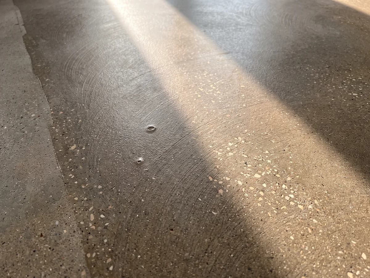 A lightly ground concrete floor under a topical sealer film, the grinder's overlapping arcs still faintly readable through the satin coat.