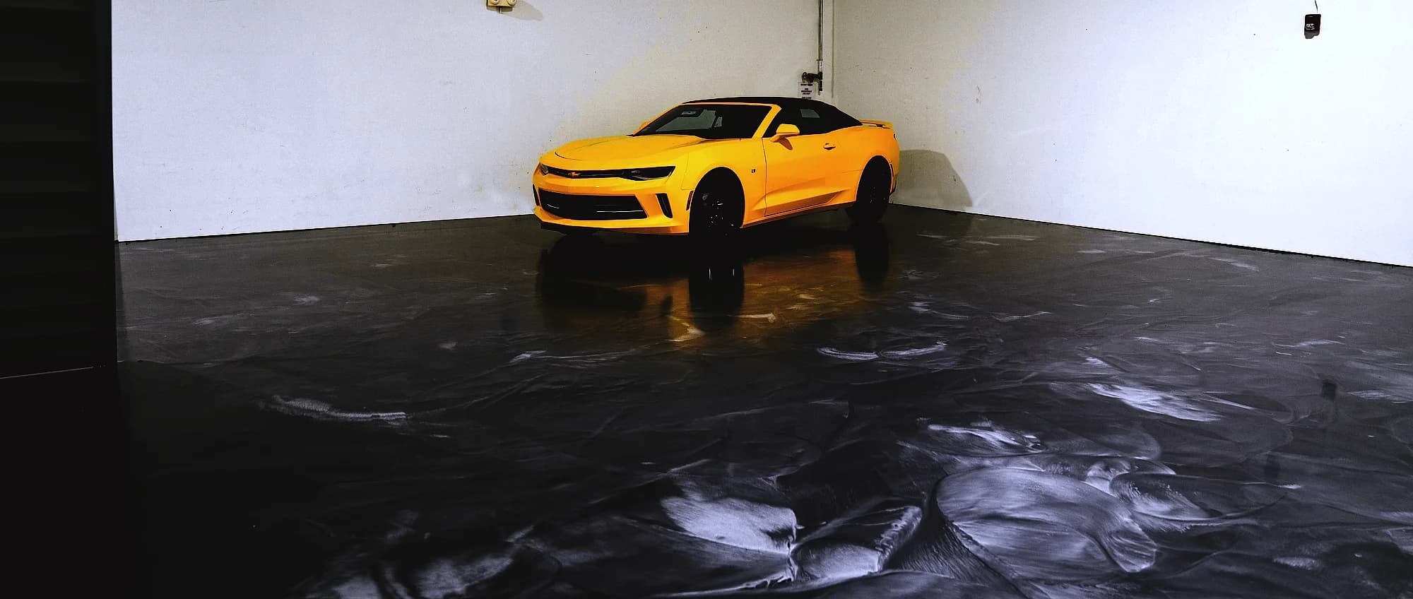 Charcoal metallic epoxy garage floor holding the reflection of a yellow sports car parked against the far wall