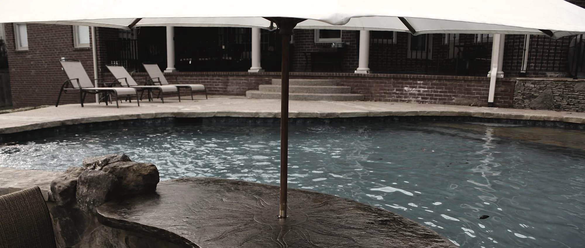 Textured sealed concrete pool deck with loungers along the house edge and the pool in the foreground