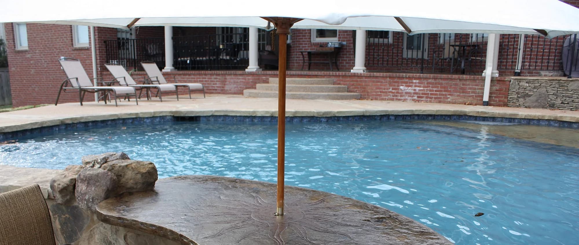 Textured sealed concrete pool deck with loungers along the house edge and the pool in the foreground