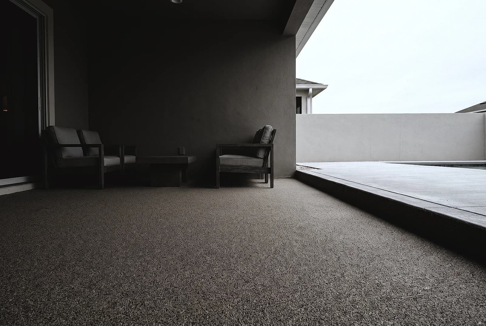 Quartz sand broadcast floor with a fine granular texture across a covered lanai, outdoor lounge chairs against the back wall