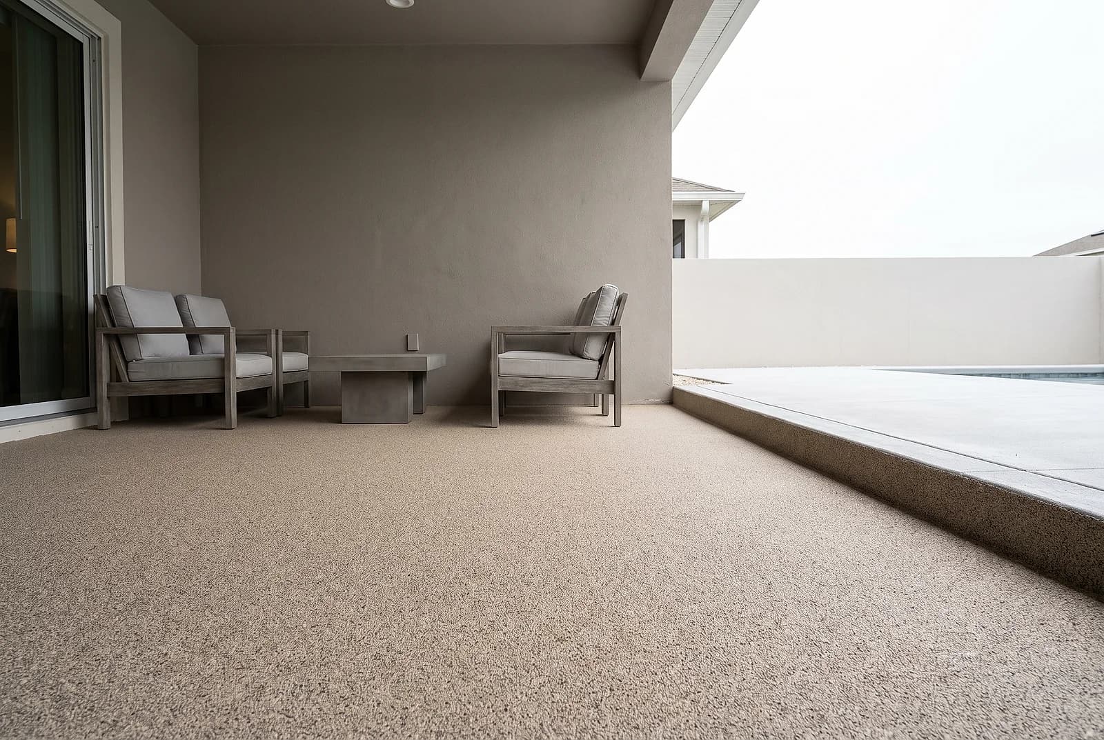 Quartz sand broadcast floor with a fine granular texture across a covered lanai, outdoor lounge chairs against the back wall