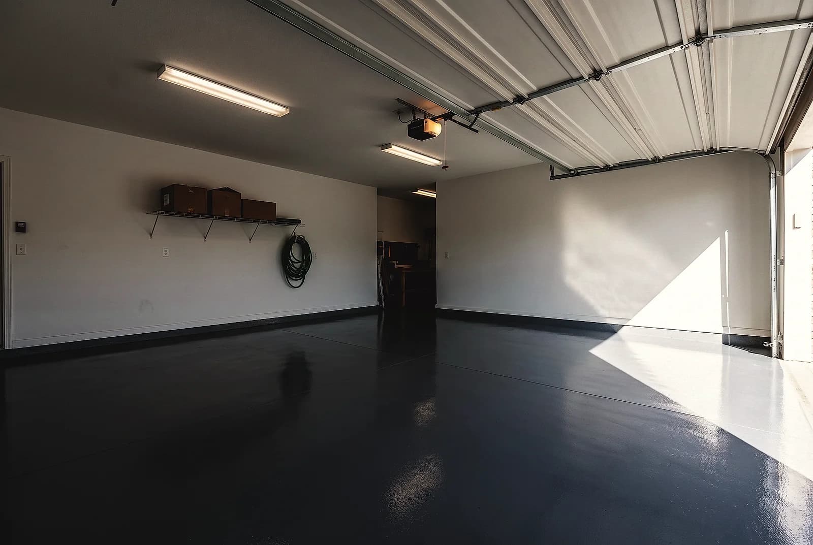 Single-color mid-gray epoxy floor with a high gloss across a two-car garage, roll-up door open to daylight