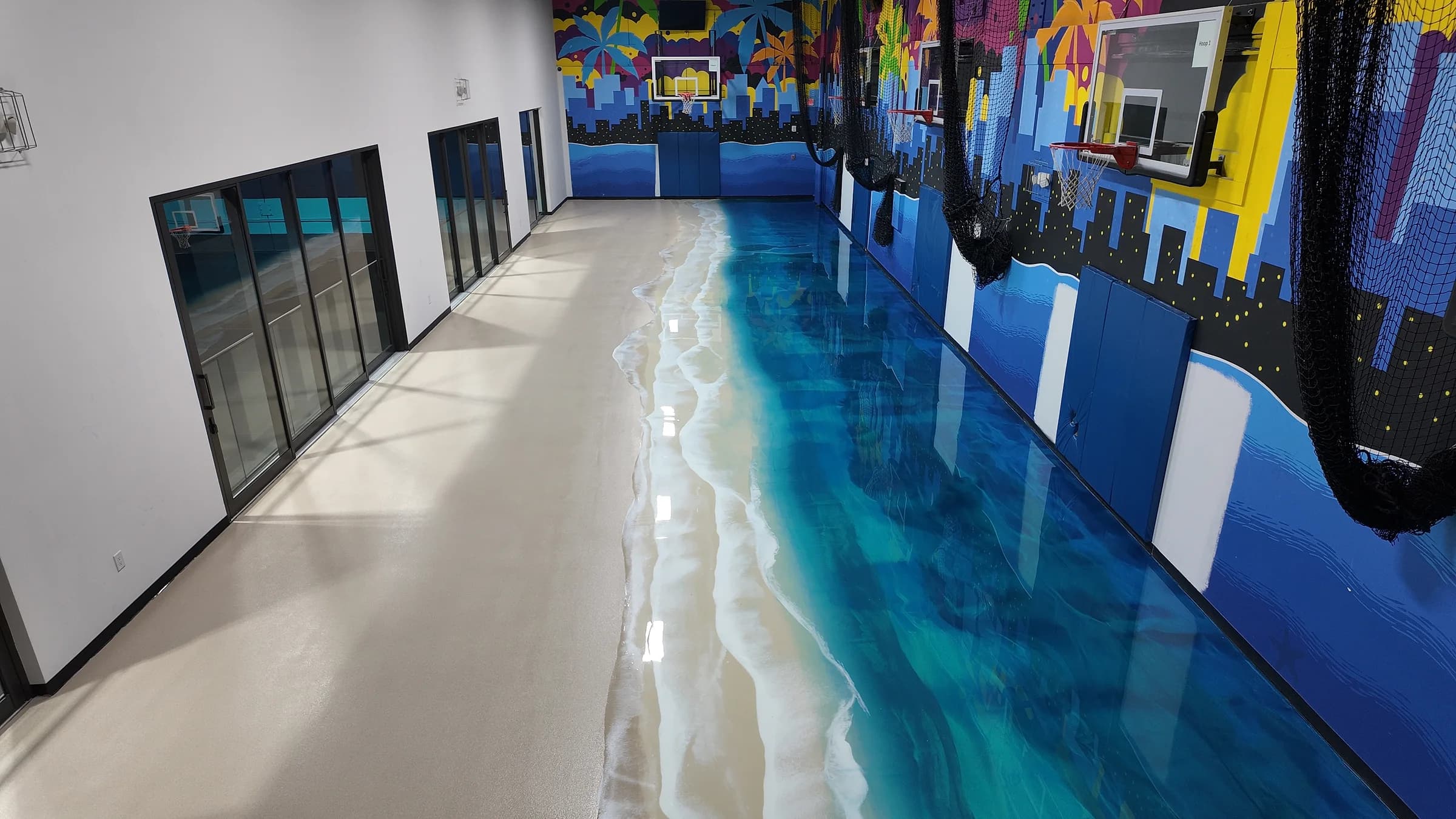 Indoor basketball court in Deerfield Beach after installation: the metallic epoxy floor poured as a beach and ocean along the murals