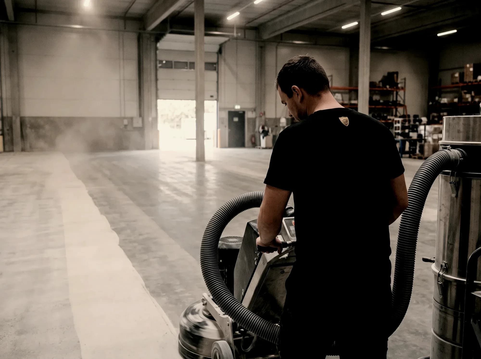 Crew member running a floor grinder with dust extraction, taking the slab down to bare concrete