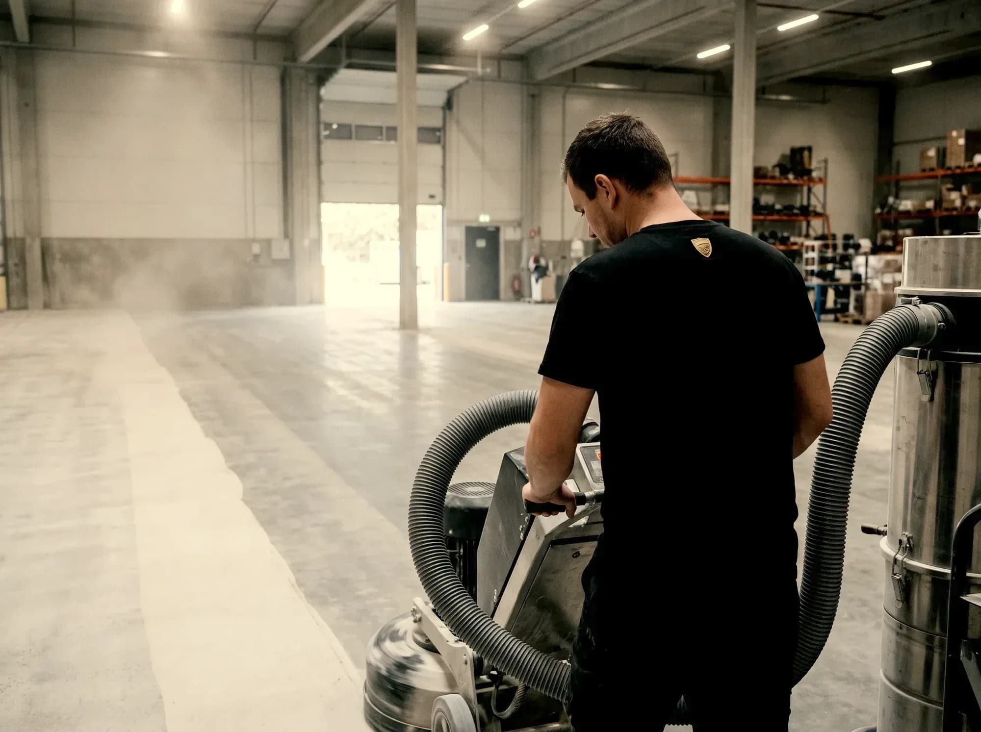 Crew member running a floor grinder with dust extraction, taking the slab down to bare concrete