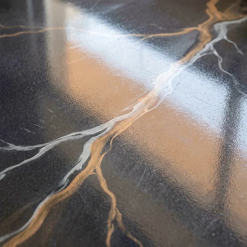 Metallic epoxy floor in a lightning-strike effect, pale pewter and brass forks branching across a near-black graphite ground.