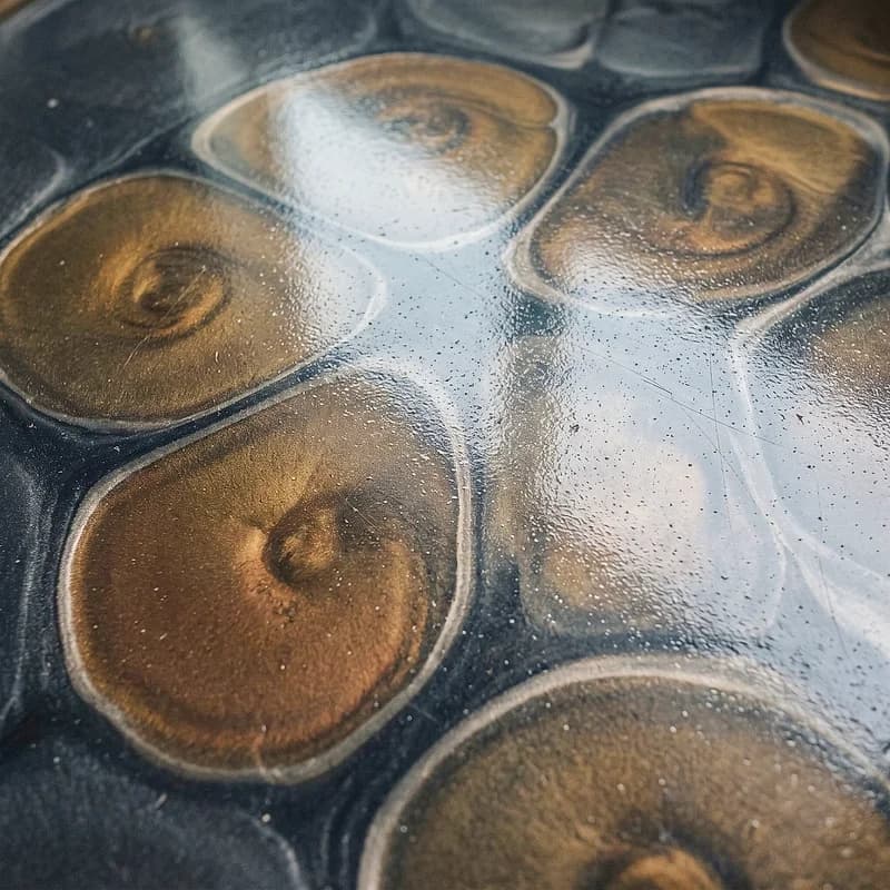 Metallic epoxy floor in a lava-lamp effect, rounded brass and bronze cells floating on a dark graphite ground.