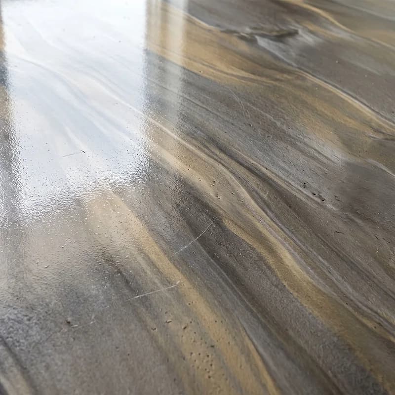 Metallic epoxy floor in a liquid-metal effect, long pewter and brass ribbons folding over one another.