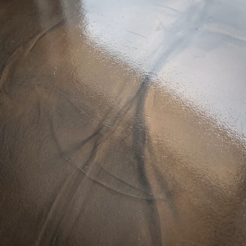Metallic epoxy floor in a tinted-glass effect, a translucent bronze-grey tint with soft veils sitting at different depths.