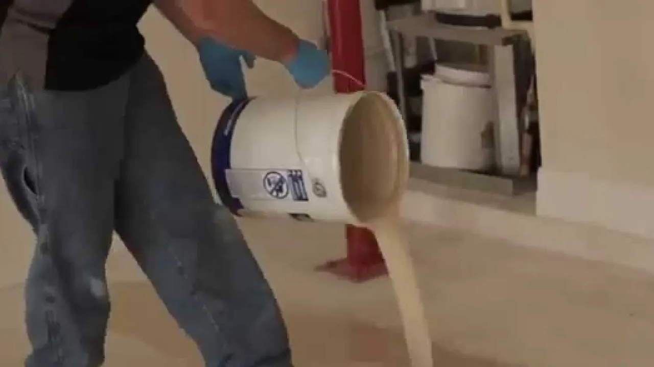 An installer tipping a bucket of coating onto a floor, the pour running out across the slab in front of him