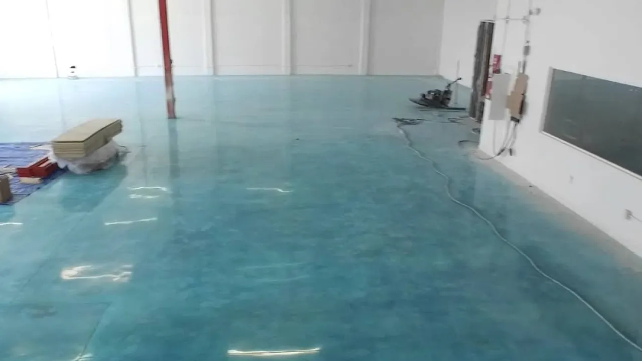 A wide turquoise-dyed polished floor filling a finished unit, the ceiling lights standing in it end to end