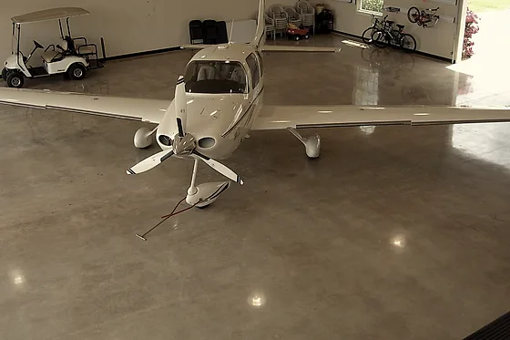 A single-engine aircraft and a ground cart parked on a warm-toned epoxy floor in a private hangar