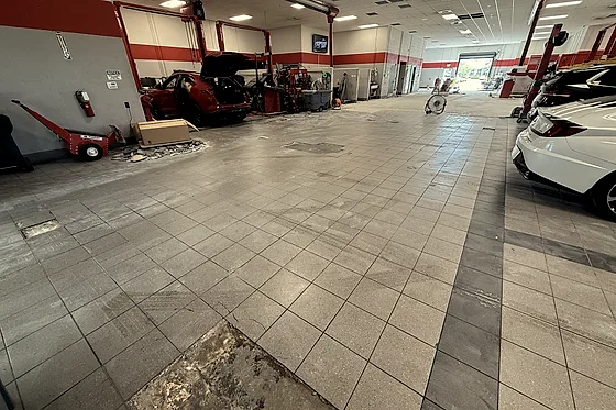 The service floor as it was, grey tile with a darker tile band and a broken patch where tiles had already come up, cars standing in the bays