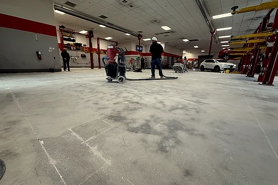 The tile gone and the bare slab being worked, a walk-behind floor machine standing on it down the service bays