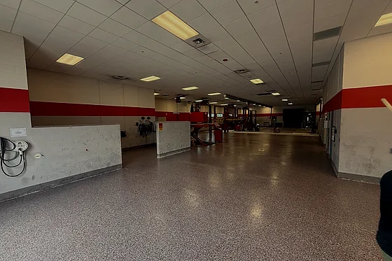 A gray flake floor running the length of a dealership service corridor past the service bays, a red band painted along the wall above it