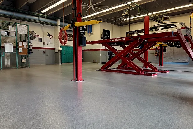 A quartz floor running the length of an automotive training bay, with a car raised on a red scissor lift and a two-post lift standing on the finished surface