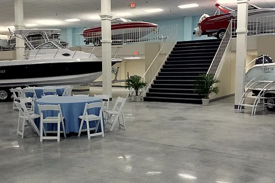 Boats on trailers standing on a polished concrete showroom floor beside laid tables, with the mezzanine stair behind