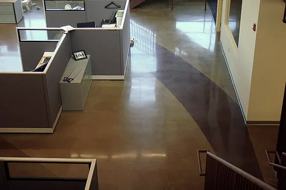 A warm amber stained polished floor sweeping past cubicle partitions in an occupied open-plan office