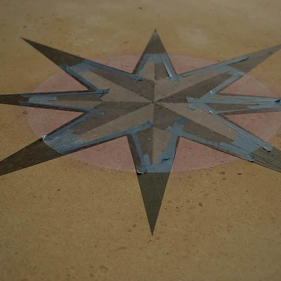 The compass star on the yellow stained floor, its points still masked with layout tape
