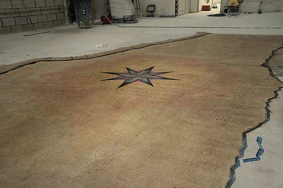 The stained floor with the compass star centred in it, masking still taped along the edge of the pour