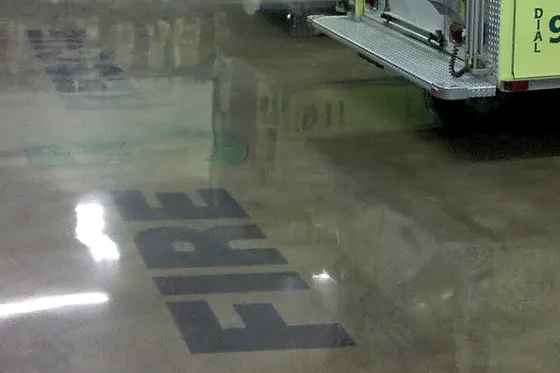 A fire engine standing in an apparatus bay on the finished polished floor, with lettering set into the slab in front of it