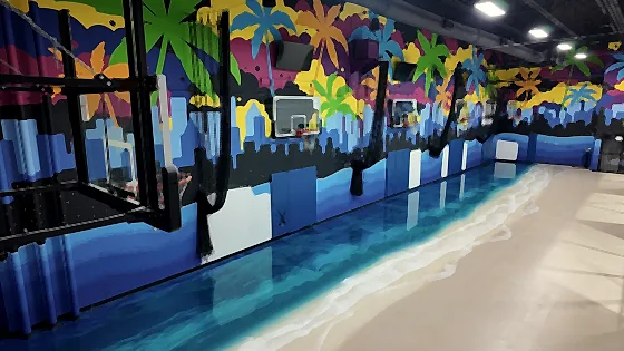 The same court seen along its length, the poured shoreline curving away under the murals and hoops