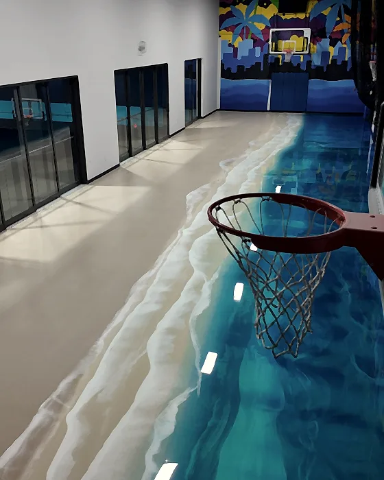 The shoreline edge of the floor meeting a pale surround, with a hoop and the glazed wall above it
