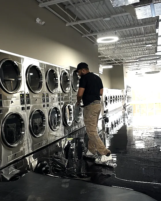 The same black floor seen down the length of the machine aisle toward the daylight, the coat still wet